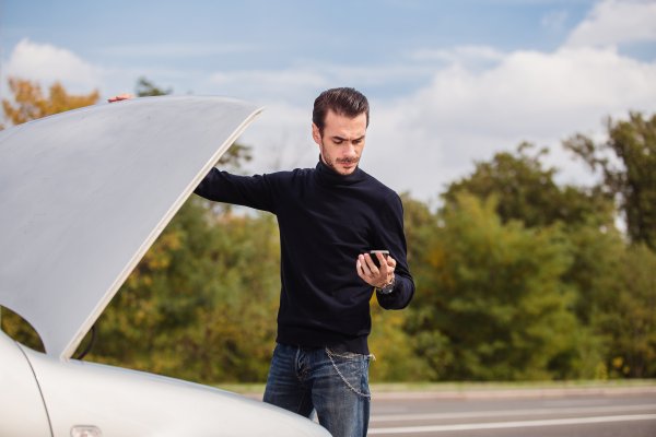 carchex features extended car warranty provider car broke down man in black sweater holds phone and open hood 